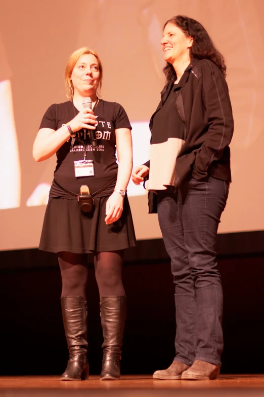 two women are talking on stage with the power point on