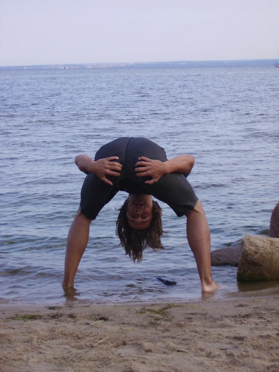 person doing yoga downward stand on beach in front of water