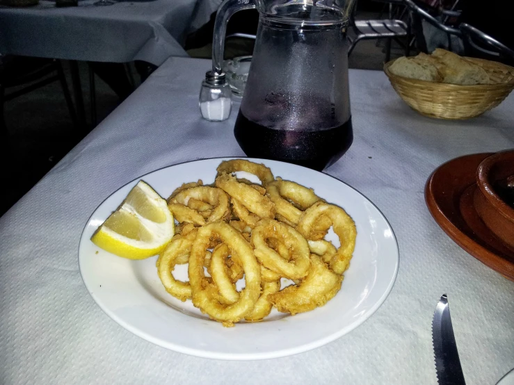 a plate with onion rings, lemon wedges and a beverage