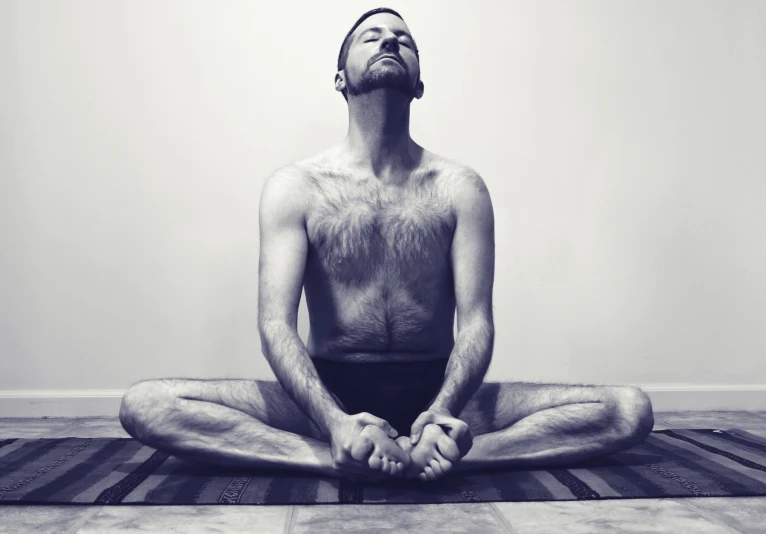 man in white underwear sits in lotus with his eyes open