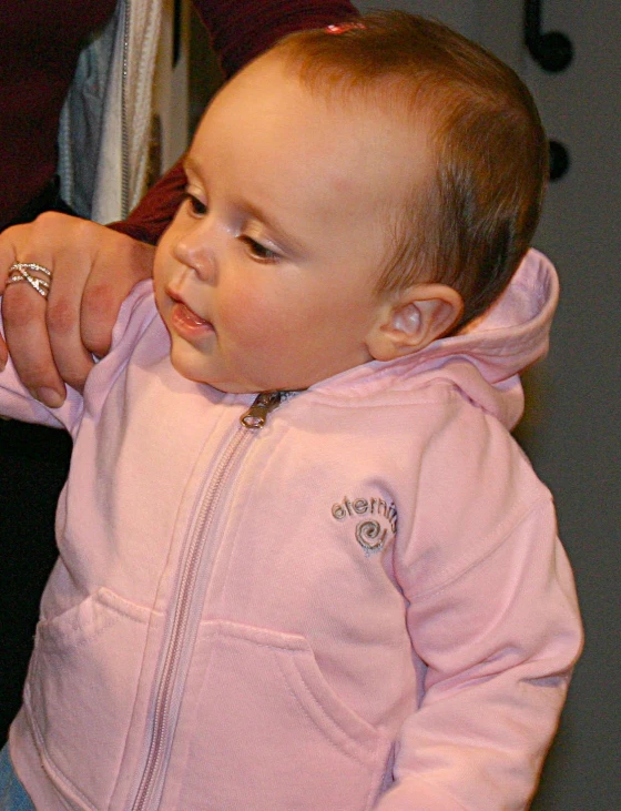 a baby girl in a pink jacket putting on ear rings