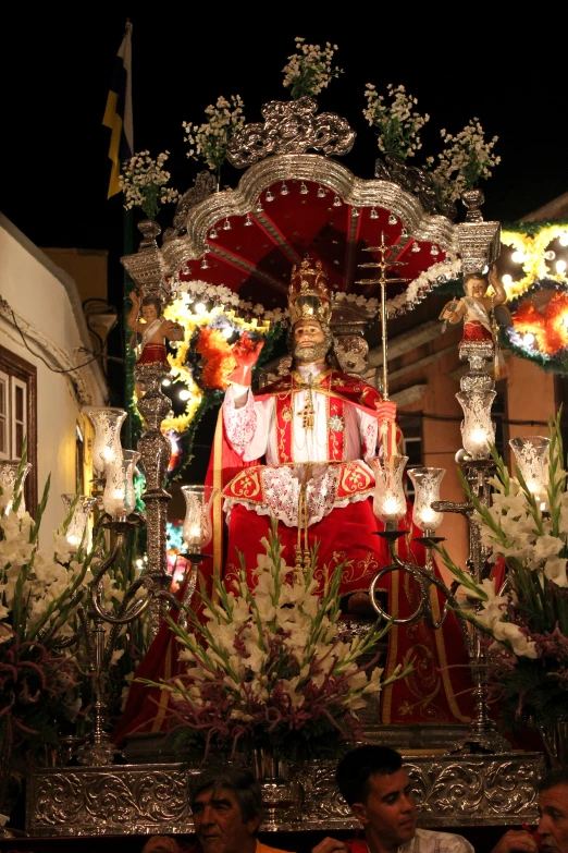 a lit up statue at night in the middle of flowers