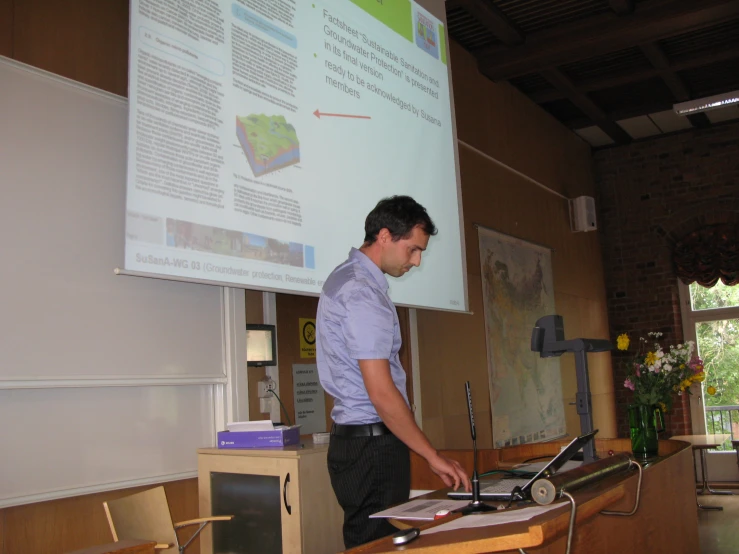 man uses a laptop computer as he stands in front of a projection screen