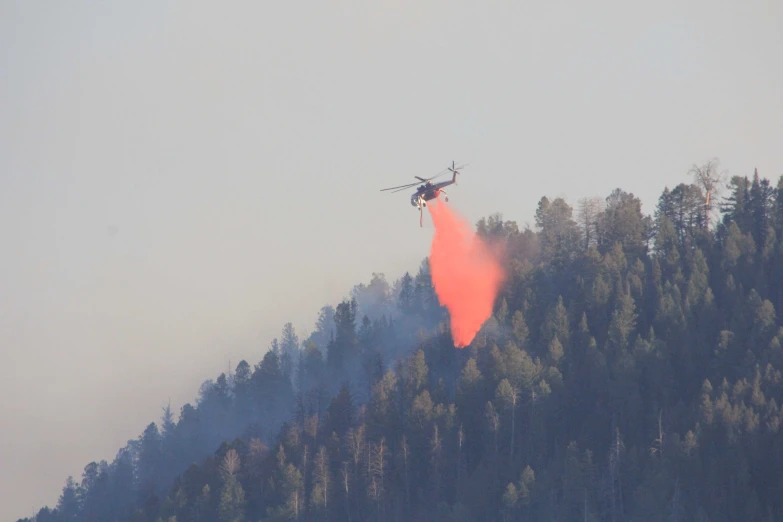 a helicopter sprays water on a tree covered mountain