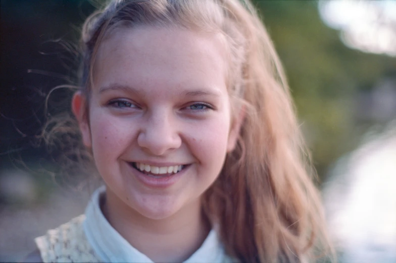 a little girl with blonde hair smiling and looking at the camera