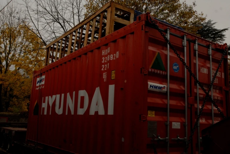 a red box car on railroad tracks with trees in background