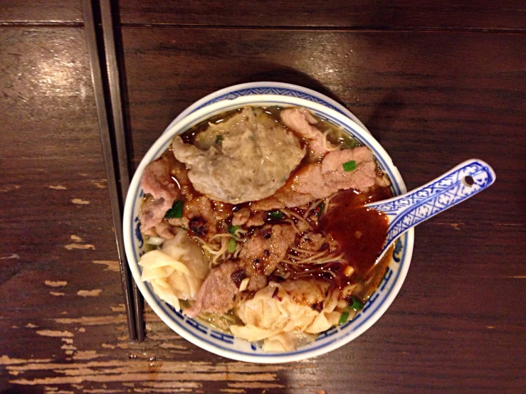 an oriental bowl filled with beef and dumplings next to a fork