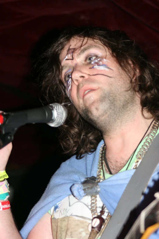 a man wearing makeup and singing into a microphone