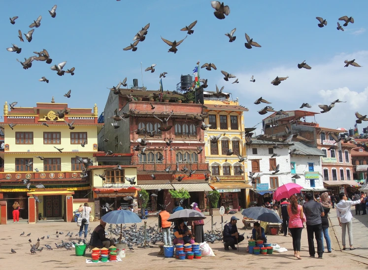 many people are standing and eating on the beach with flying birds