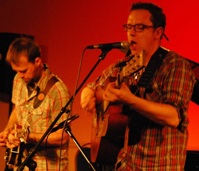 a man playing guitar while another sings on the microphone