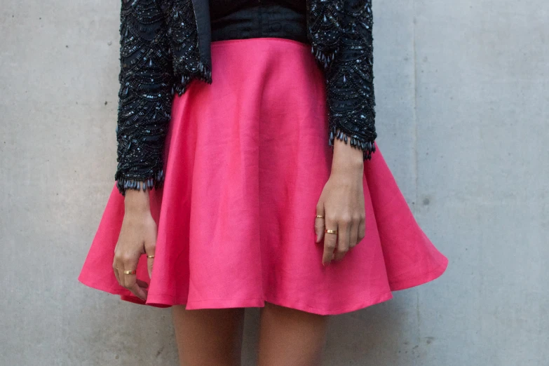 a woman standing against a wall wearing a skirt and jacket