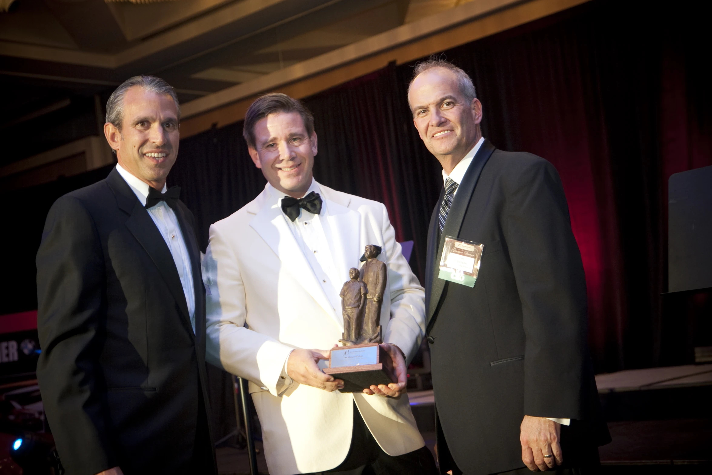 three men standing in front of a stage holding an award