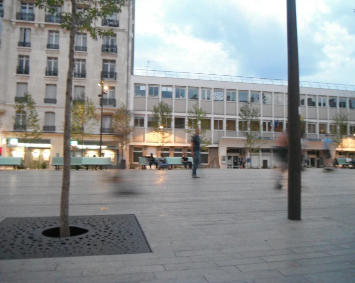 an empty plaza with two trees and a man walking by
