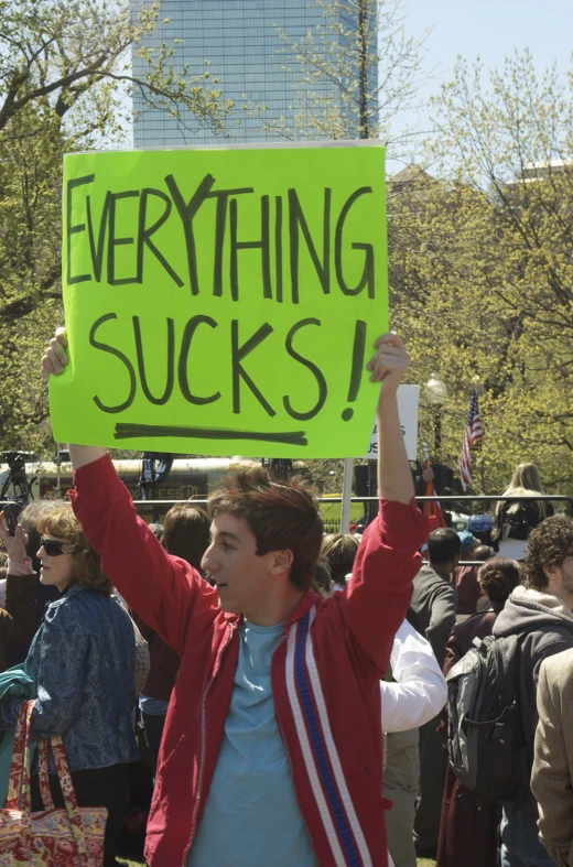 a man holding up a green sign reading everything sucks