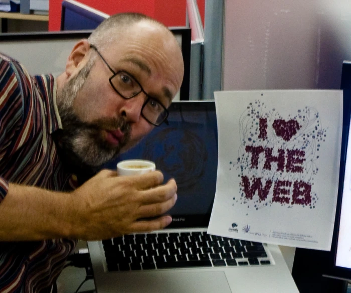 man holding cup looking at artwork displayed on laptop