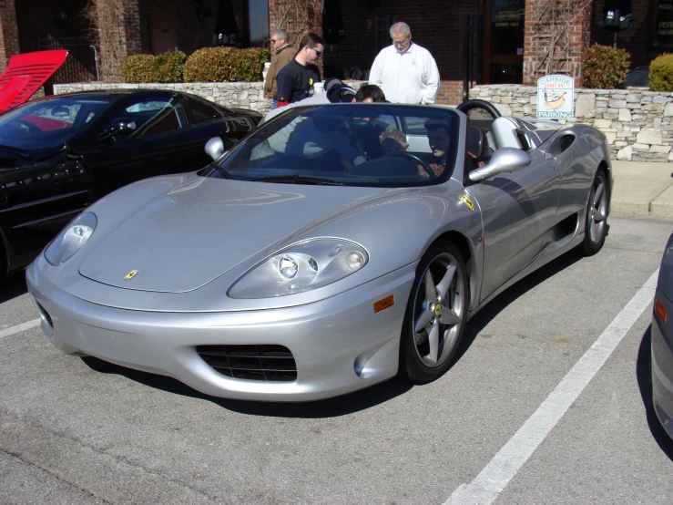 silver car sitting in parking lot with people standing nearby