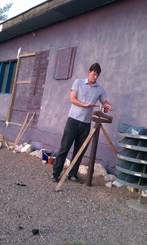 a man leaning against a wooden post with a tool