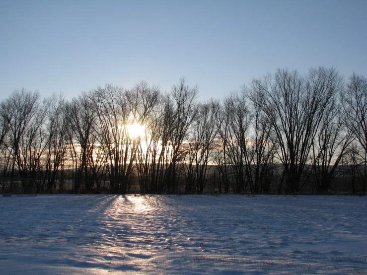the sun is setting over the snow covered woods