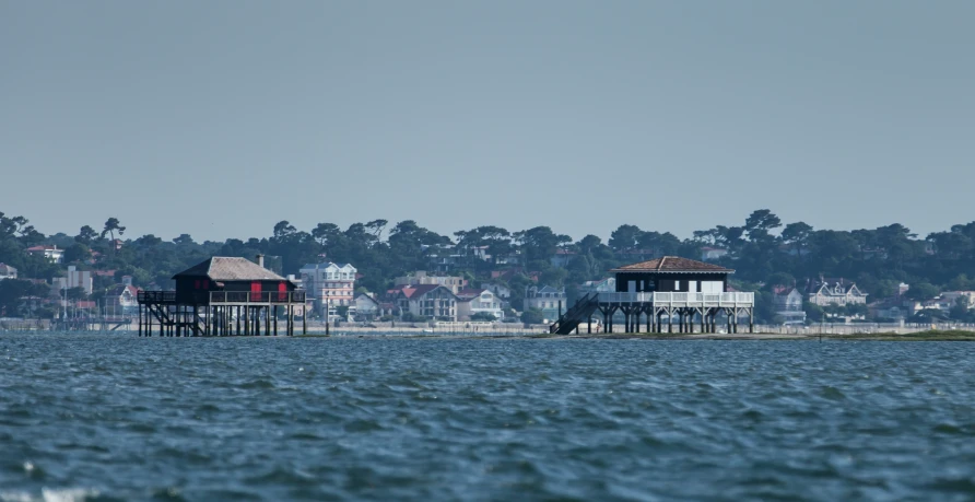 three shacks on stilts with blue ocean in front