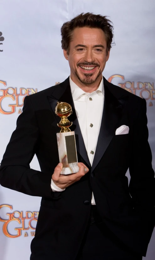 the man in a tuxedo is posing with a golden globe