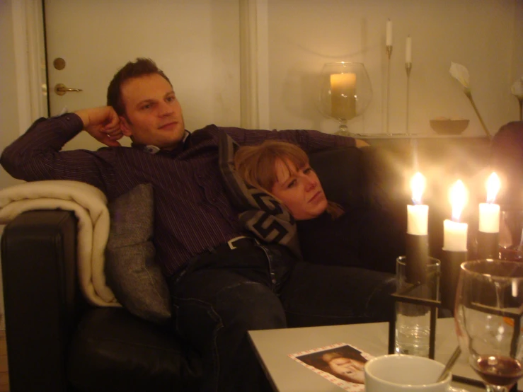 two people on a couch, with one person holding his head while the other holds his hands near the head and has his eyes close to the camera