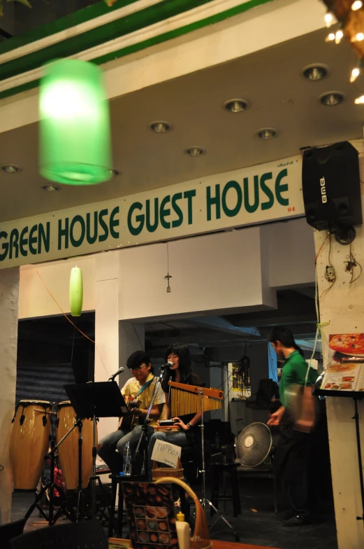 group of people play music under a green house guest house sign