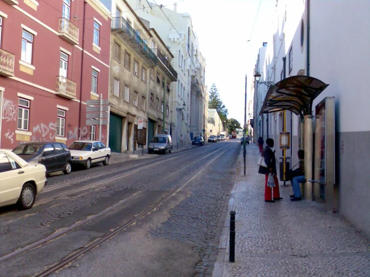 street scene with people standing at entrance to bus stop and parked cars