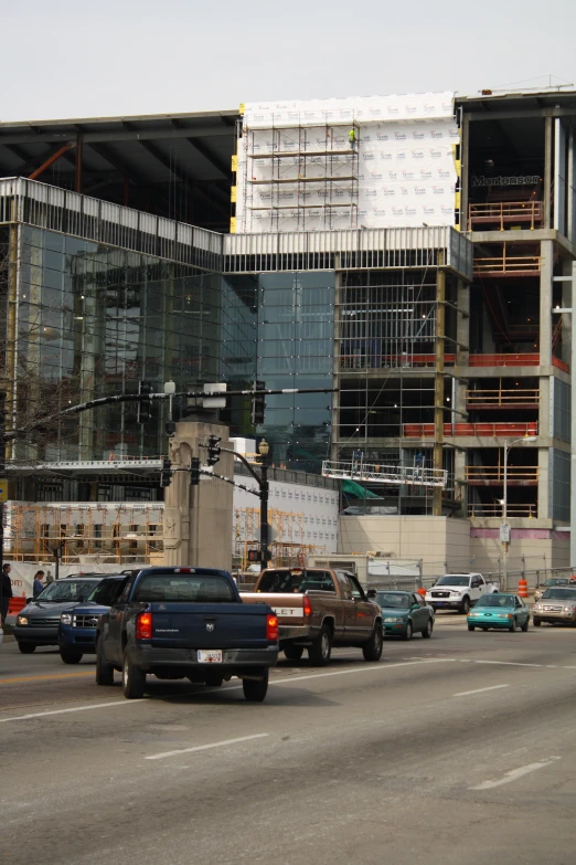 a group of cars driving by construction with a big building in the background