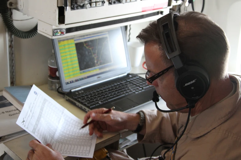 a man sits at his desk looking through papers with headphones on