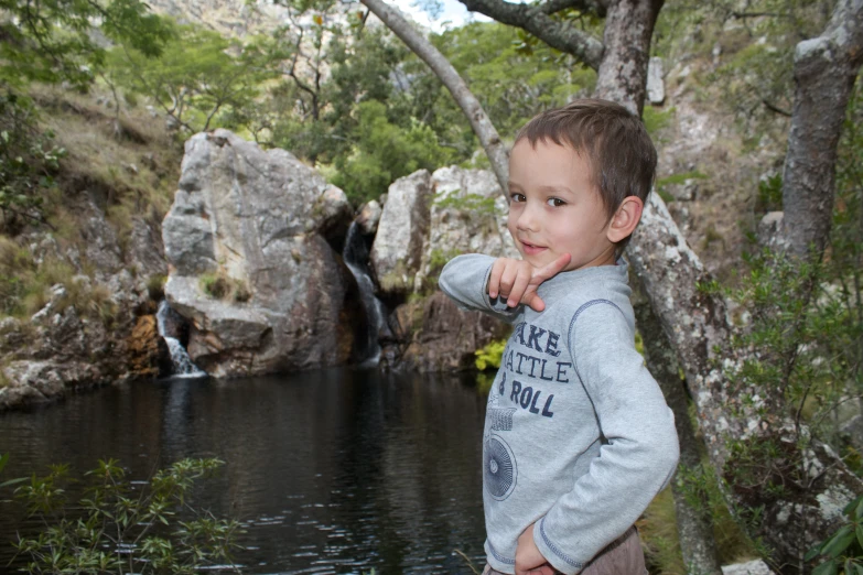 a boy poses for a po in front of a lake