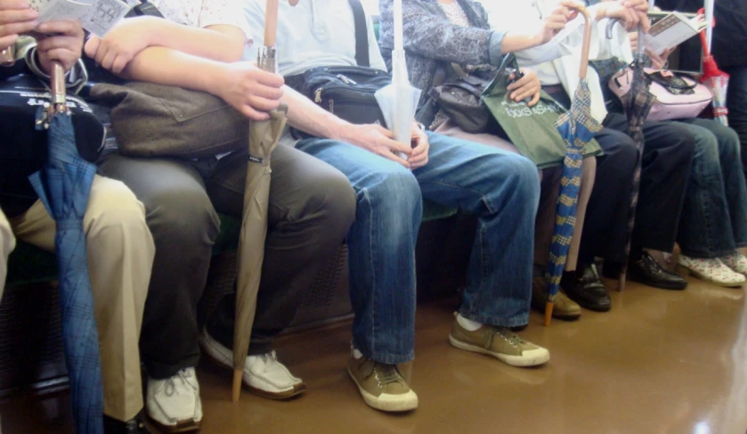 group of people sitting on a public transportation with umbrellas