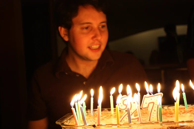 a man looking at a birthday cake with candles lit