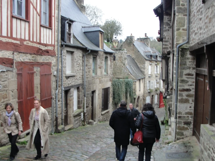 several people walk on a cobblestone street next to small stone buildings