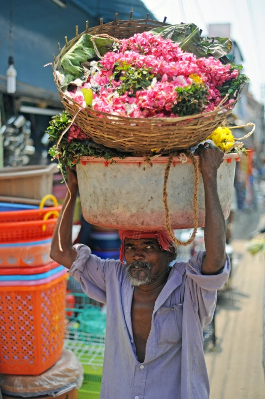 the man carries a large basket of flowers over his head