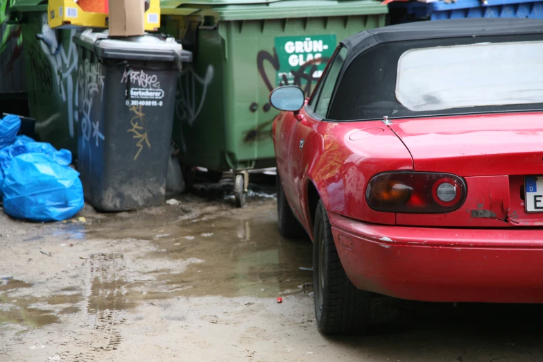 red car parked next to trash cans in front of it