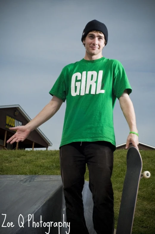 a man in green shirt holding a skateboard on top of a ramp