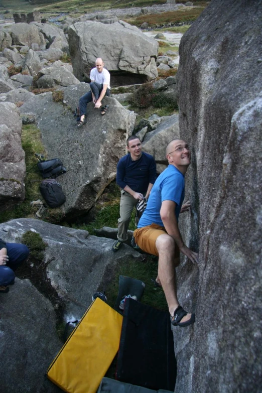 four people sitting on rocks together while one is trying to climb