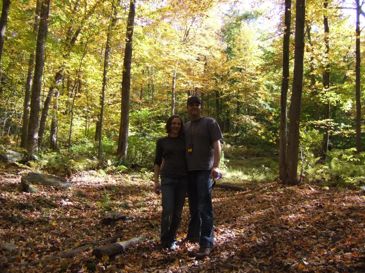 the man and woman are standing in leaves in the forest