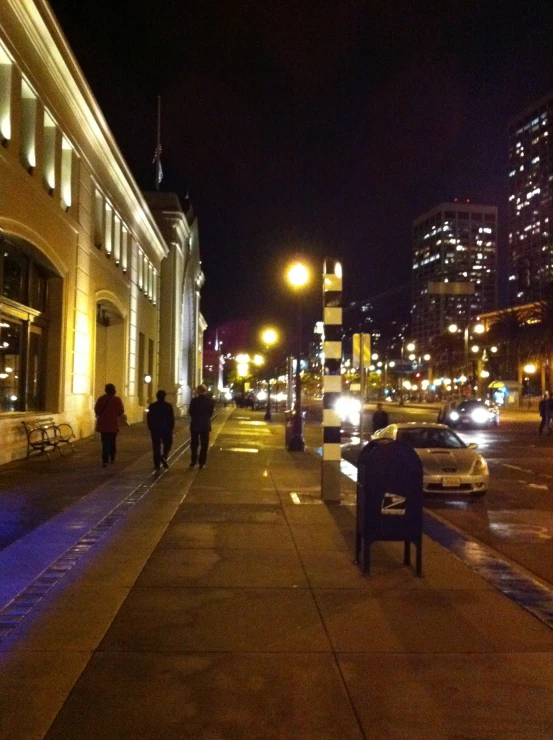 people are walking on the sidewalk outside of a city at night