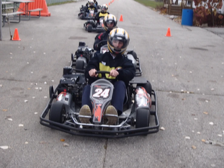 three people ride their small race car down a paved road