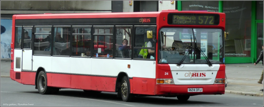 a red, white and black bus driving past a tall building