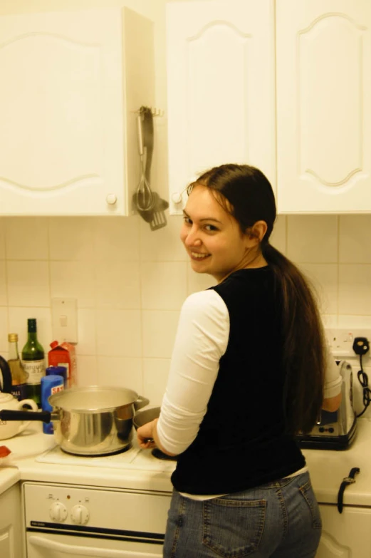 young woman in kitchen with pot and lid, posing for camera