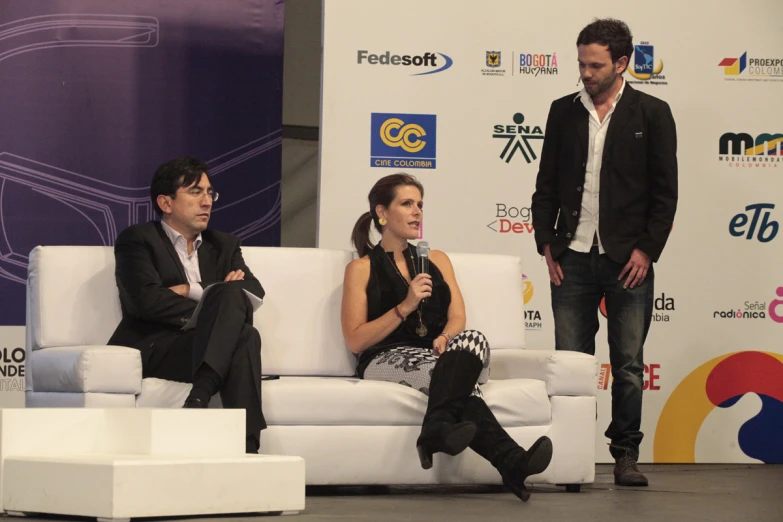 a man and a woman on white couches speaking at the event