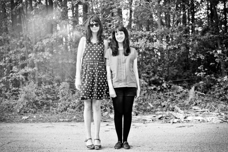 two women standing next to each other in front of some trees