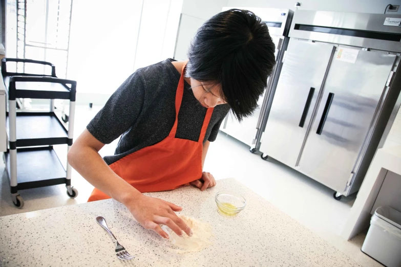 a woman in an orange apron rolls up dough