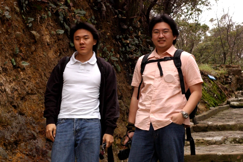 two asian males are standing near a tree