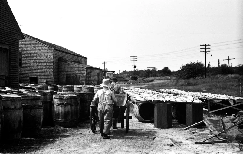 man in hat carrying luggage near barrels and barn