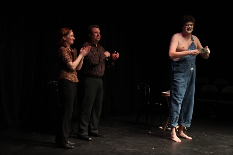 three people stand on stage with one holding up soing