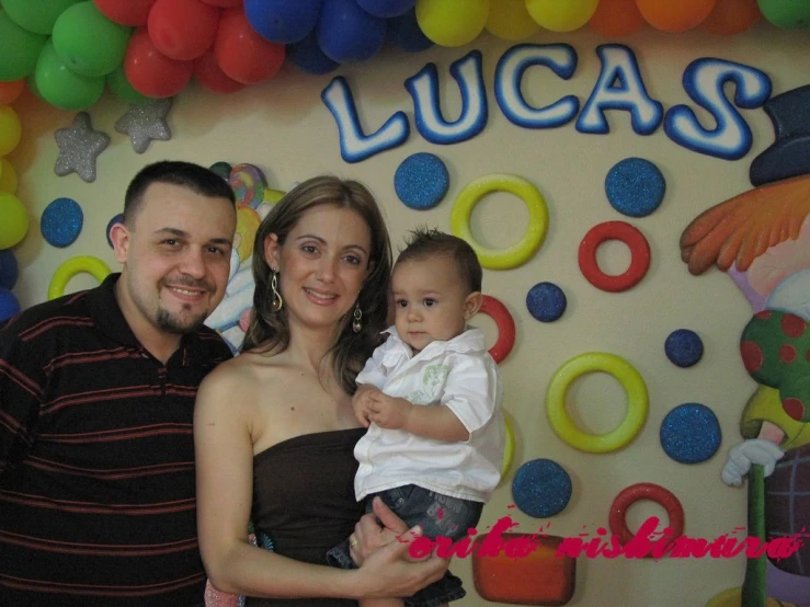 a couple pose with their baby in front of a bunch of balloons