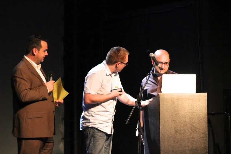 three men standing around an podium with microphones